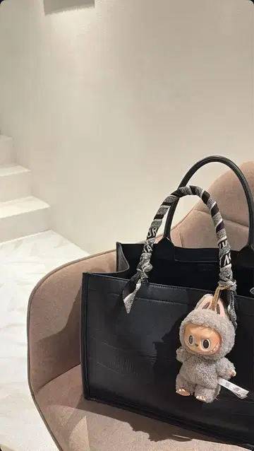검은색 핸드백에 인형이 달려 있습니다.