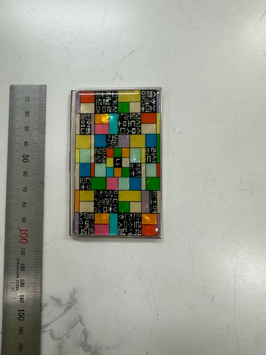 전통적인 나전칠기 기법을 현대적으로 재해석하여 형색 각색의 화려한 자개 조각을 모자이크처럼 담아낸 전면과, 정교한 전통 문양 및 KOREA' 각인이 돋보이는 명함케이스